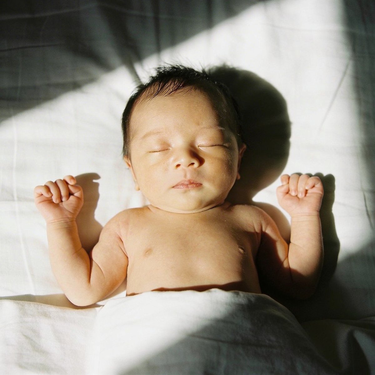 Nouveau-né allongé baigné d'une lumière de fenêtre douce, photographié sous angle rasant